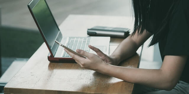 una mujer con su tlf y laptop buscando en línea.